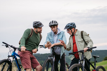 Grandfather, father and teen boy on cycling trip looking at map in smartphone.
