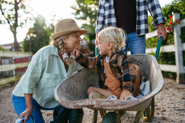 Grandmother playing with grandson in a wheelbarrow on a family farm.