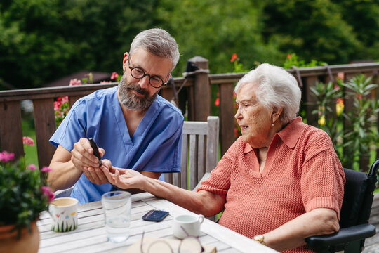 Nurse helping elderly woman measure blood sugar with glucometer.