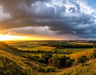 Fototapeta premium Expansive landscape showing rolling hills and fields bathed in warm sunlight, contrasted by dramatic, stormy clouds