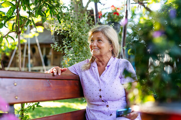 Senior woman sitting in garden, scrolling on phone.