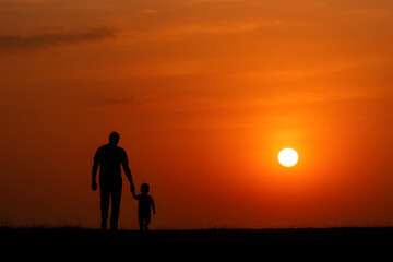 Fototapeta premium Father and child walking hand in hand at sunset, silhouette symbolizing love and family bond