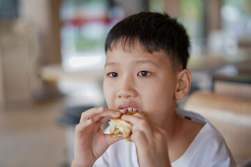 young boy is eating a sandwich, Asian boy is happily eating food