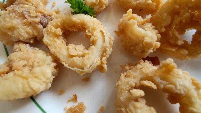 A close-up image of golden crispy fried calamari rings served on a white plate. This popular seafood appetizer is made from squid coated in seasoned flour and deep-fried until crunchy