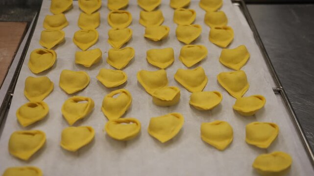 Close‑up of hands arranging uncooked tortelli on a parchment‑lined tray, neatly placed in rows, highlighting artisanal pasta craftsmanship in Italy.