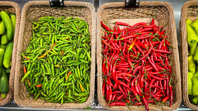 Green and red chili peppers are arranged in baskets on a market stall. Natural ingredients and a culinary contrast of flavors.