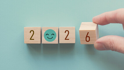 Hands holding 2026 with smile face wooden blocks, Happy New Year, positive mental health plan, optimistic resolution goal, eco sustainable target concept