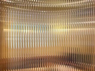 Close up texture of fluted glass, or striped glass, with the refraction of gold backgrounds and yellow lights behind it. Fluted glass is aesthetically beautiful. Seamless background texture.