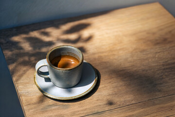 espresso coffee shot serving in small mug on wooden table in sun light and shade of wood branches and leaves