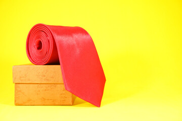 Red tie rolled on gift box closeup view on yellow background 