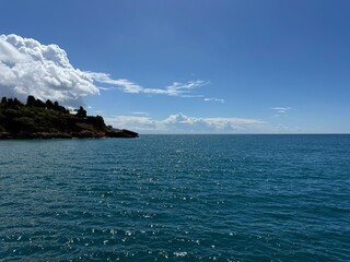  Sea blue glittering water, sunny sky and rocky coastline.