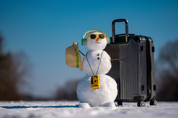 Snowman traveler with suitcase and headphones. Winter music. Funny snowman listening to music. Snowman with earphones. Winter music. Snowman celebrating with music and travel gear. Christmas songs.