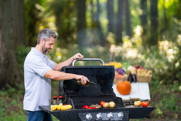 Handsome middle-aged Hispanic man grilling meat on a backyard barbecue. Fit millennial chef cooking...