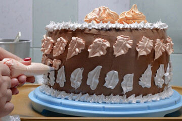 A woman pastry chef with a pastry bag in her hands squeezes cream on a cake in a home kitchen. Professional chef at work on bakery kitchen. culinary, baking and cooking food concept, home cooking
