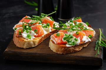 Salmon sandwiches, salted fish,  cream cheese and green onion on wooden background. Healthy breakfast with salmon toasts