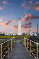 Grotta Lighthouse in Seltjarnarnes near Reykjavik, Iceland, stands beyond a rope lined path and volcanic rocks in soft evening light with pastel clouds and calm sea.