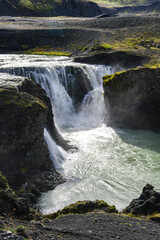 Late afternoon light reveals textured rock and layered cascades in a remote Iceland highland canyon, with mist rising as water squeezes through a narrow chute.