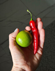 A hand cradles fiery red chili and zesty lime, evoking a spicy tango, ideal for Dia de los Muertos...