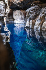 Electric blue water fills a narrow fissure in Thingvellir National Park, Iceland, reflecting cavern walls. Soft daylight reveals basalt layers and vivid clarity between plates.