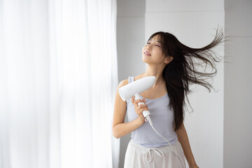 Young Woman Drying Hair with Hair Dryer at Home