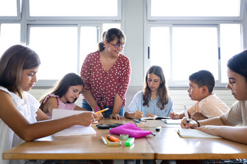 Fototapeta premium Teacher helping elementary school students studying in classroom