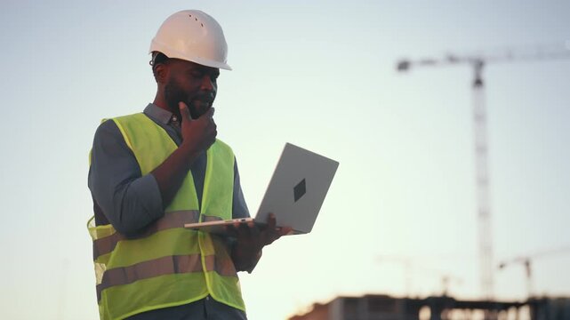 Modern technology and software for architect and builders, black man with laptop . Inspector or auditor checking quality of building, professional engineer on construction site, african ethnicity