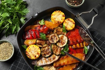 Delicious grilled vegetables in pan and spices on dark table, flat lay