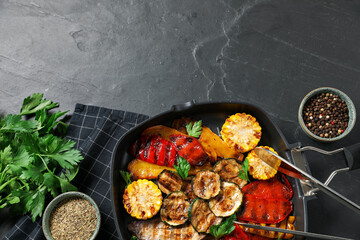 Delicious grilled vegetables in pan and spices on dark textured table, flat lay. Space for text