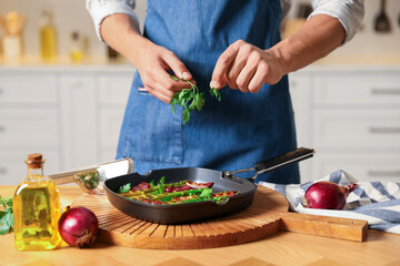 Man adding parsley into pan with grilled vegetables at table indoors, closeup