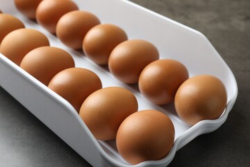 Raw chicken eggs in plastic container on grey table, closeup