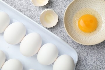 Many whole raw chicken eggs and broken one in bowl on grey table, flat lay
