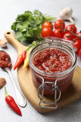 Tasty salsa sauce in jar and ingredients on light table, closeup