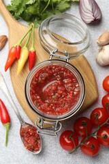 Tasty salsa sauce in jar and ingredients on light table, flat lay