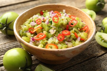 Tasty salsa in bowl and green tomatoes on wooden table, closeup