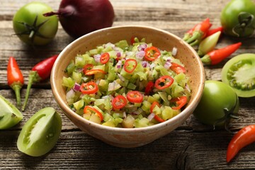 Tasty salsa in bowl and ingredients on wooden table, closeup