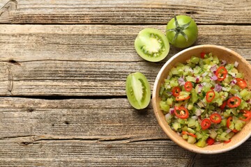 Tasty salsa in bowl and green tomatoes on wooden table, flat lay. Space for text