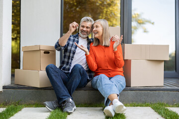 Senior couple sitting at front door with keys enjoying new property