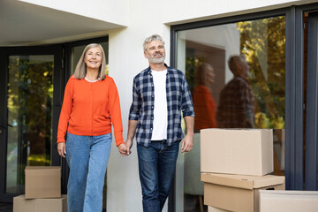Senior man with gray hair and wife smiling holding hands near moving boxes