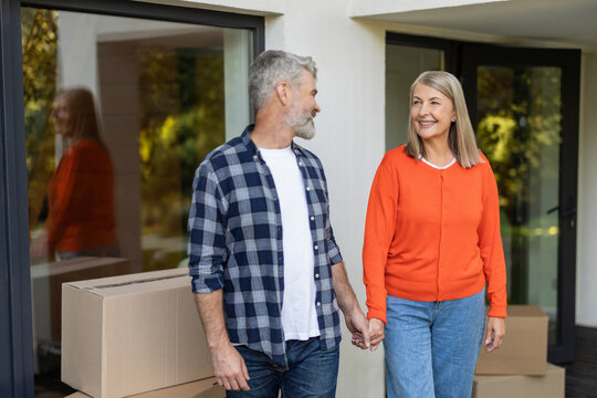 Senior couple celebrating relocation holding hands near home entrance - Powered by Adobe