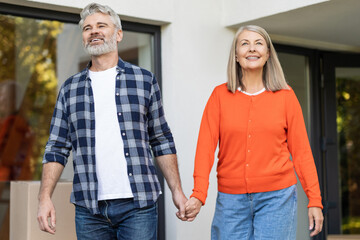 Senior couple standing with packed boxes behind holding hands