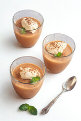 Three glasses of gazpacho soup with creamy topping and basil garnish