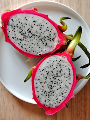 Top view of a fresh dragon fruit cut in half on a white plate.