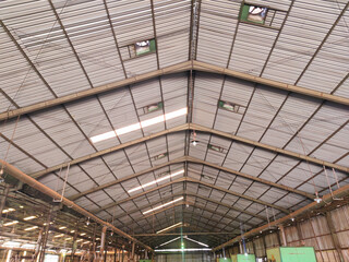 A wide-angle view of an aging factory roof structure made of steel framing, long ventilation strips and natural light openings, giving a sense of height and industrial scale