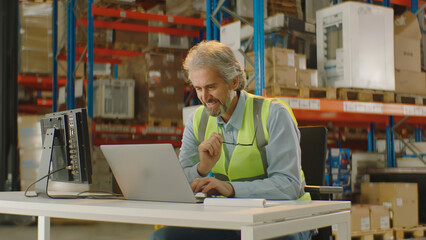 Senior warehouse manager using laptop checking operations