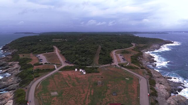 Aerial view of Conanicut Island and Beavertail Lighthouse in Beavertail State Park at the entrance to Narragansett Bay. The camera dolly out over the tip of the island and lighthouse on a cloudy day.