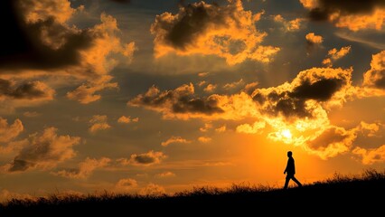 Obraz premium Silhouette of a person walking along a hill at sunset, against an orange sky filled with clouds. Concept Silhouette Portraits, Sunset Photography, Hilltop Landscape, Orange Sky and Clouds