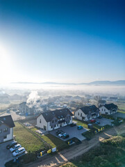 Nowoczesny dom na osiedlu z widokiem na błękitne niebo. Jasna elewacja, duże okna i prosta forma podkreślają współczesny styl architektury. Ujęcie oddaje harmonię między nowoczesnym budownictwem a spo © Freshfanpage