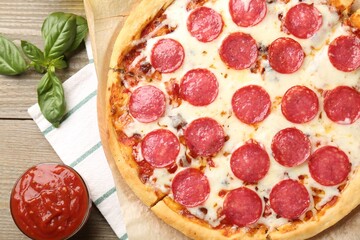 Delicious pepperoni pizza served with tomato sauce on wooden table, flat lay