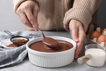 Woman with liquid chocolate dough in bowl at grey table, closeup