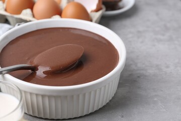 Liquid chocolate dough in bowl and ingredients on grey table, closeup. Space for text